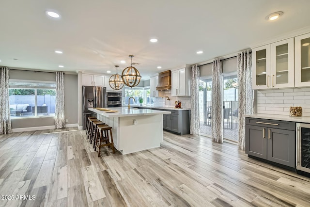 kitchen with an island with sink, custom exhaust hood, stainless steel fridge, pendant lighting, and gray cabinetry