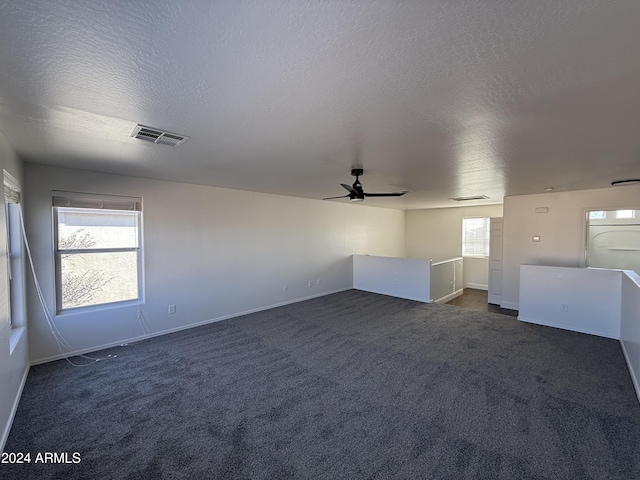 spare room featuring ceiling fan, a textured ceiling, and dark colored carpet