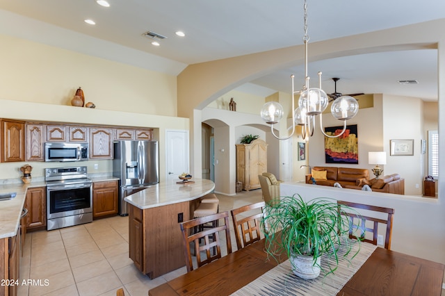 kitchen featuring light tile patterned flooring, hanging light fixtures, vaulted ceiling, a kitchen island, and stainless steel appliances