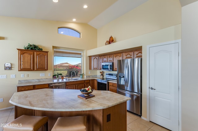 kitchen with appliances with stainless steel finishes, light tile patterned floors, a kitchen island, and lofted ceiling