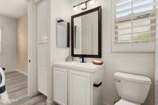 half bathroom with vanity, wood finished floors, toilet, and baseboards