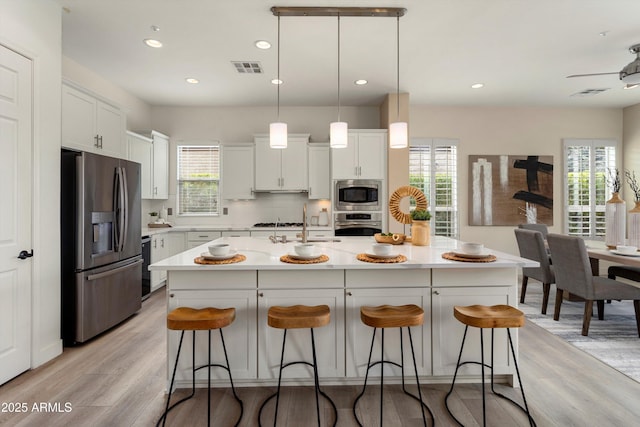 kitchen with stainless steel appliances, a kitchen bar, light countertops, and white cabinets