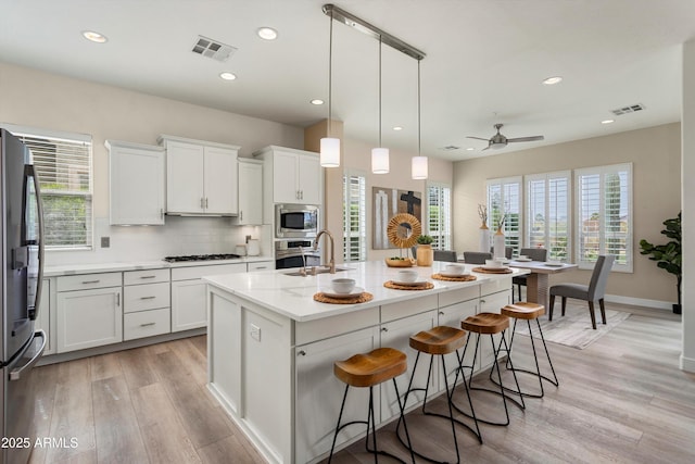 kitchen with light wood finished floors, stainless steel appliances, decorative backsplash, white cabinetry, and a sink