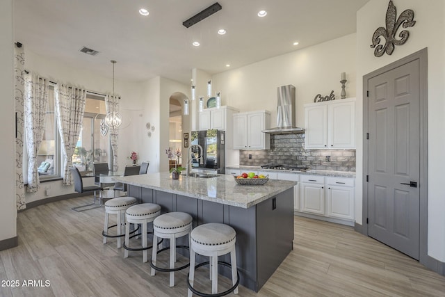 4915 N Greentree Dr, Litchfield Park, AZ 85340 - kitchen with wall chimney range hood, white cabinetry, a kitchen island with sink, stainless steel gas cooktop, and decorative light fixtures