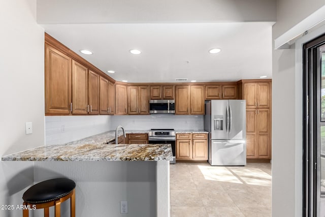 kitchen featuring a kitchen bar, appliances with stainless steel finishes, kitchen peninsula, light stone countertops, and backsplash