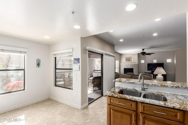 kitchen featuring light stone counters, ceiling fan, and sink