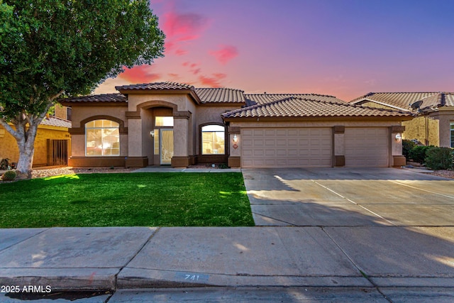 mediterranean / spanish house featuring an attached garage, a tile roof, concrete driveway, stucco siding, and a front yard