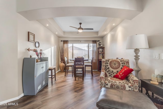 living area featuring dark wood-type flooring, ceiling fan, and a raised ceiling