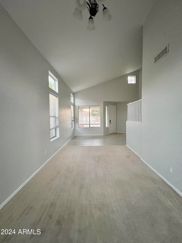 carpeted spare room featuring high vaulted ceiling and a chandelier