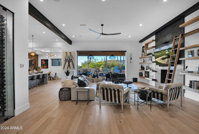 living room featuring a fireplace, beam ceiling, light hardwood / wood-style floors, and ceiling fan