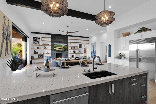 kitchen with stainless steel built in refrigerator, sink, hanging light fixtures, a fireplace, and white cabinetry