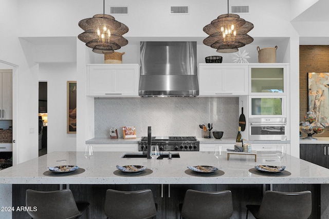 kitchen with pendant lighting, wall chimney exhaust hood, stainless steel appliances, and a kitchen island with sink