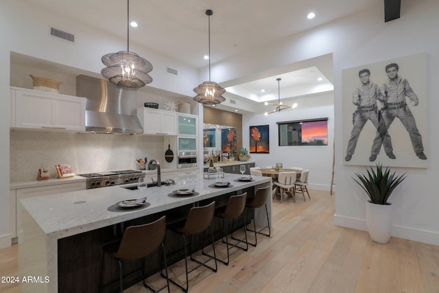 kitchen with sink, wall chimney exhaust hood, light wood-type flooring, white cabinetry, and stainless steel appliances