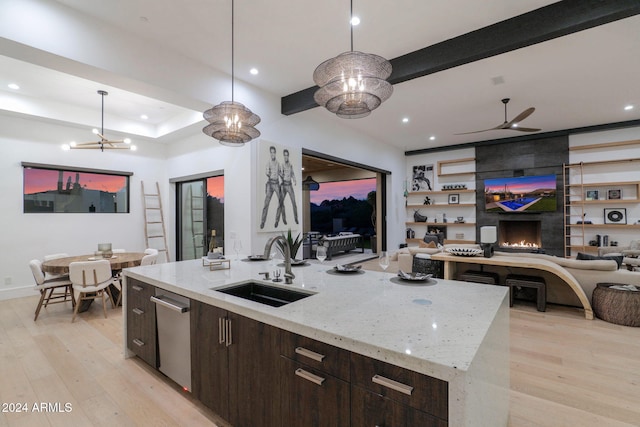 kitchen featuring light stone countertops, a large fireplace, sink, decorative light fixtures, and a kitchen island with sink