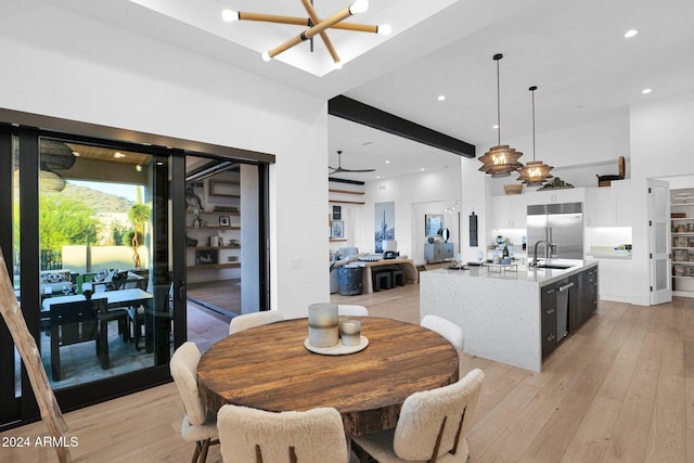 dining area featuring beam ceiling, sink, light hardwood / wood-style floors, and ceiling fan with notable chandelier