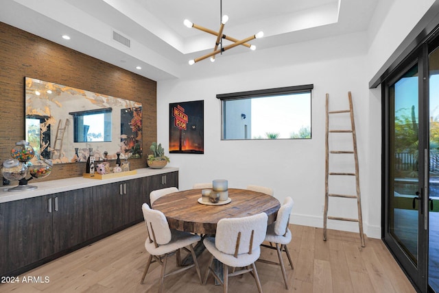 dining space featuring a chandelier, light wood-type flooring, and a raised ceiling