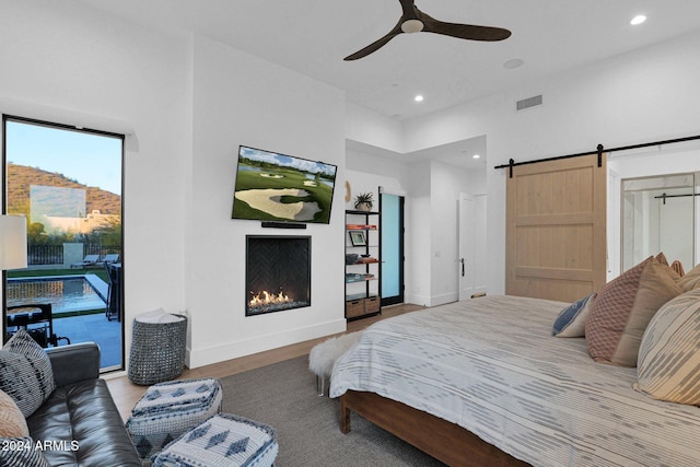 bedroom with hardwood / wood-style floors, ceiling fan, a barn door, and access to outside