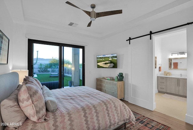 bedroom with access to outside, ensuite bath, ceiling fan, a barn door, and light hardwood / wood-style floors