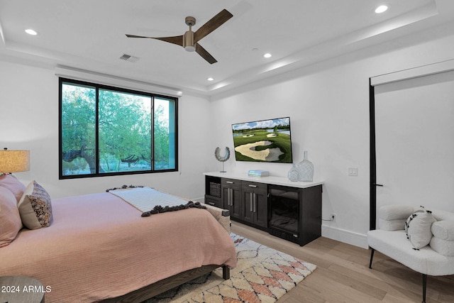 bedroom featuring a raised ceiling, ceiling fan, and light hardwood / wood-style flooring