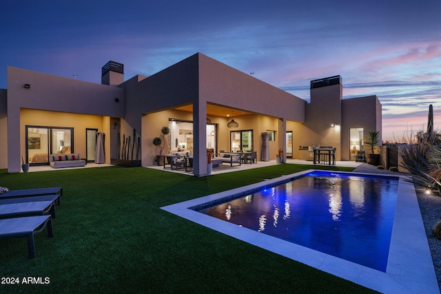 back house at dusk with outdoor lounge area, a patio area, and a lawn