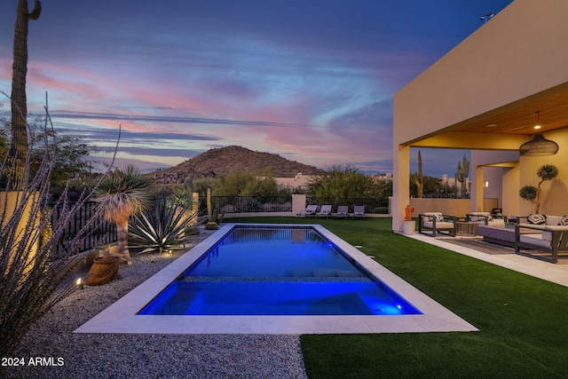 pool at dusk featuring a mountain view, an outdoor living space, a yard, and a patio