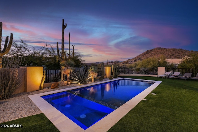 pool at dusk with a mountain view, an in ground hot tub, and a lawn