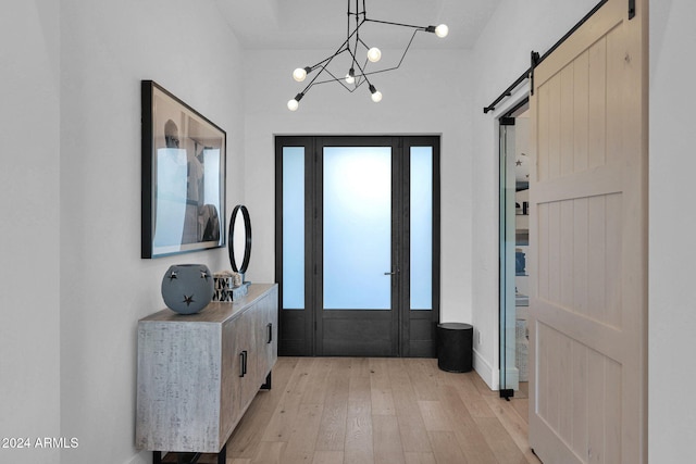 entryway with a barn door, light hardwood / wood-style floors, and an inviting chandelier