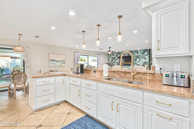 kitchen with sink, white cabinetry, hanging light fixtures, light stone counters, and kitchen peninsula