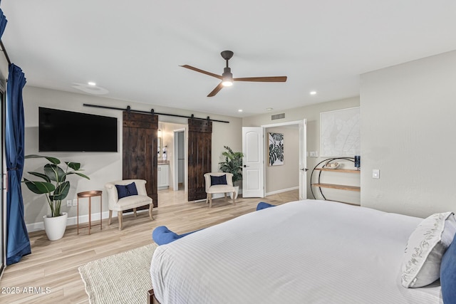 bedroom featuring ceiling fan, a barn door, and light hardwood / wood-style flooring