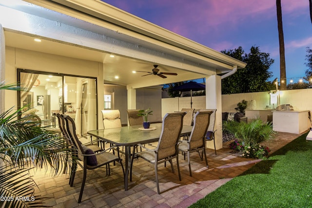 patio terrace at dusk featuring ceiling fan and exterior kitchen