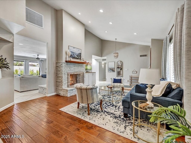 living room featuring a stone fireplace, high vaulted ceiling, ceiling fan, and light wood-type flooring