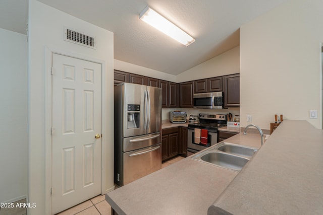 kitchen featuring lofted ceiling, stainless steel appliances, sink, light tile patterned floors, and dark brown cabinets