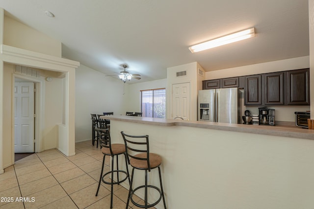 kitchen featuring ceiling fan, lofted ceiling, a kitchen bar, light tile patterned floors, and stainless steel fridge