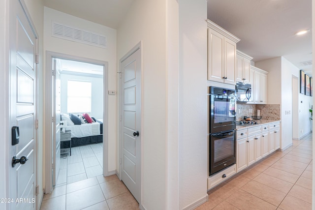 kitchen featuring black appliances, white cabinets, light tile patterned floors, tasteful backsplash, and light stone counters