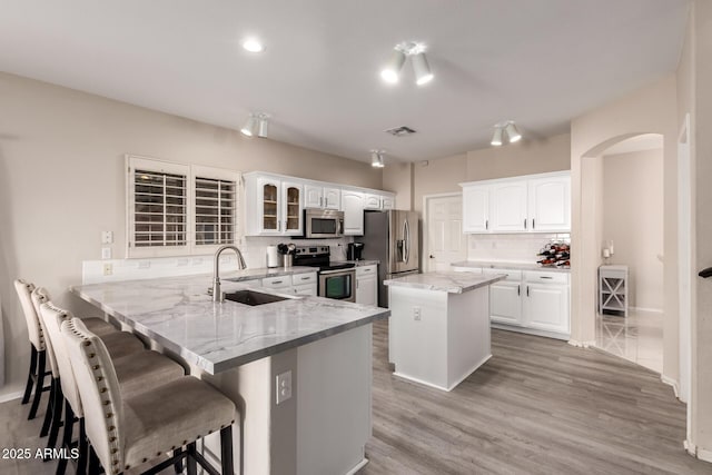 kitchen featuring white cabinets, a kitchen island, a peninsula, stainless steel appliances, and a sink