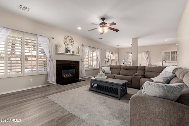 living room featuring visible vents, a ceiling fan, a high end fireplace, wood finished floors, and baseboards