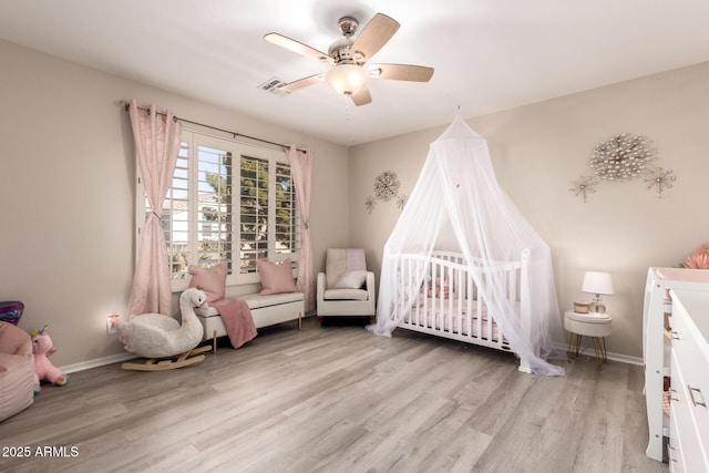 bedroom with light wood finished floors, visible vents, baseboards, ceiling fan, and a nursery area