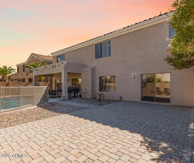 back of house at dusk featuring stucco siding, fence, and a patio