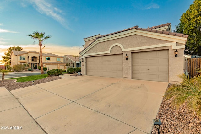 mediterranean / spanish home featuring concrete driveway, a tile roof, a residential view, an attached garage, and stucco siding