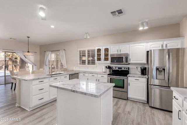 kitchen with decorative light fixtures, stainless steel appliances, a kitchen island, a sink, and glass insert cabinets