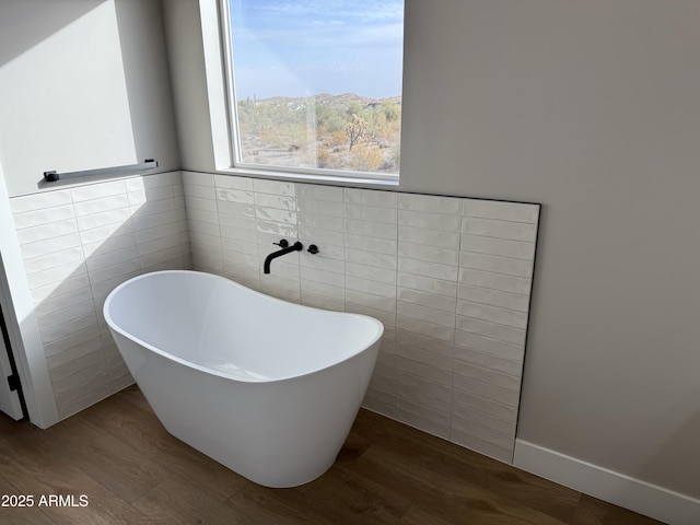 bathroom with tile walls, a tub to relax in, a mountain view, and hardwood / wood-style floors