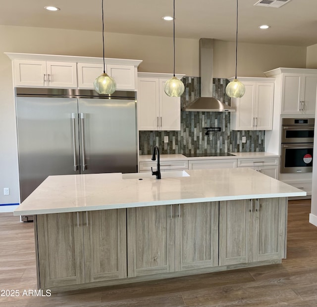 kitchen featuring a center island with sink, light stone countertops, wall chimney range hood, and white cabinets