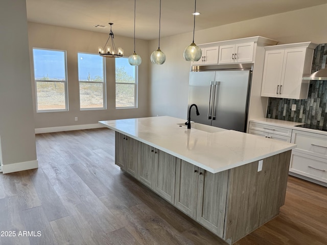 kitchen with white cabinetry, stainless steel built in refrigerator, hanging light fixtures, and a spacious island