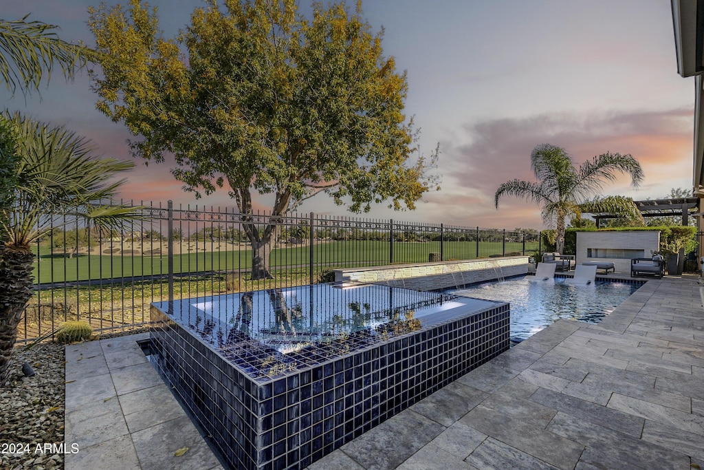 pool at dusk featuring a jacuzzi, pool water feature, and a patio