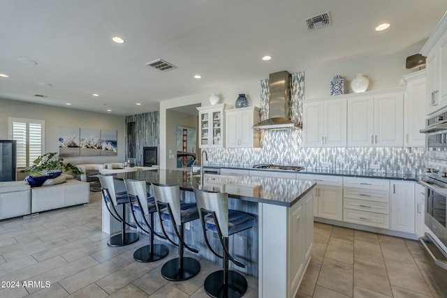 kitchen with sink, wall chimney exhaust hood, a breakfast bar area, a center island with sink, and white cabinets