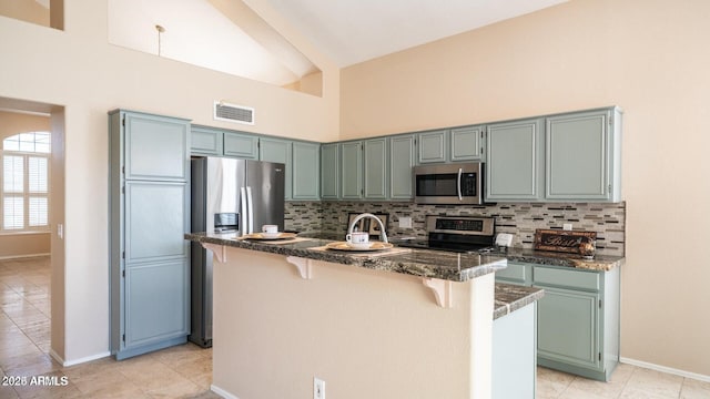 kitchen with light tile patterned floors, backsplash, stainless steel appliances, high vaulted ceiling, and a kitchen bar