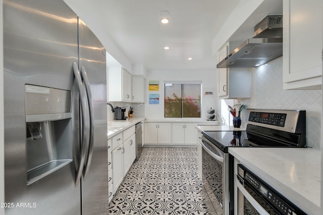 kitchen featuring white cabinets, decorative backsplash, light stone counters, stainless steel appliances, and wall chimney exhaust hood