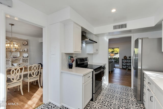 kitchen with wall chimney range hood, white cabinetry, backsplash, stainless steel appliances, and a notable chandelier