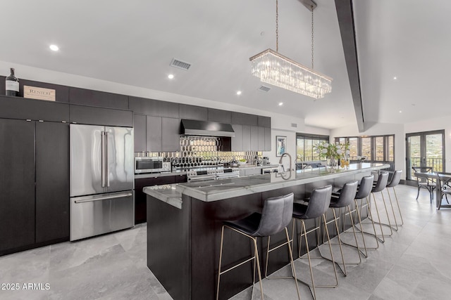 kitchen featuring premium appliances, wall chimney range hood, a spacious island, and a kitchen bar