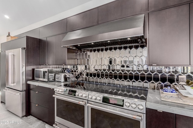 kitchen featuring high end appliances, dark brown cabinets, wall chimney range hood, and decorative backsplash